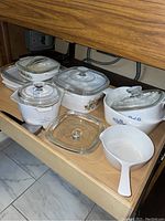 Photo showing the set of Corning Ware dishes including Cornflower Blue pattern casserole dishes with glass lids, a white measuring bowl with lid, and a bowl with handle and spout.