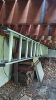Full side view of the aluminum extension ladder stored under a patio, showing the length and context of storage area.