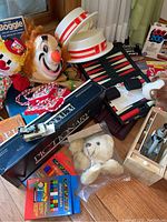 Full lot view showing board games, clown mask and hat, stuffed animals, puzzle books, and Lumex microscope box