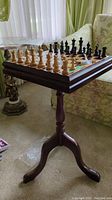 Photo of the small wooden pedestal game table with chess board set up with wooden chess pieces arranged for play.