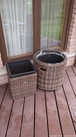 Two wicker garden urns, one cube-shaped and one cylindrical, shown on a deck outside a window.