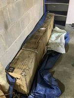 Sealed cardboard box containing gazebo parts on a blue tarp in garage