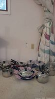 Full view of the cookware set showing saucepans, frying pans, and steamer pots with lids and handles, arranged on floor