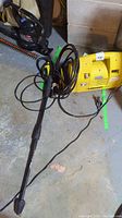 Yellow Karcher 420 pressure washer unit on floor with black power cord and wand lying next to it.