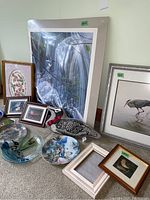 Wide view of bird-themed framed prints, decorative plates, ceramic birds and stuffed loon pillow arranged on floor against wall