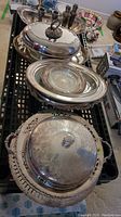 Photo showing silverplate handled tray with lid, glass-lined serving dish, candleholders, salt and pepper shakers arranged on black cart.