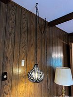 Full view of retro swag lamp hanging from ceiling chain against wood panel wall.