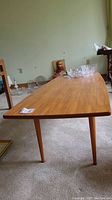 Full view of the teak coffee table from a low angle showing its rectangular shape, wood grain, and tapered legs.