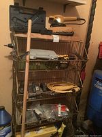 Full view of metal wire shelving unit containing various tools including electric belt sanders, extension cord, drill, tool boxes, push broom, and miscellaneous items.