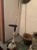 Full length view of the Stihl FS38 gas string trimmer showing white and orange motor housing, metal shaft, and handle grip, standing indoors.