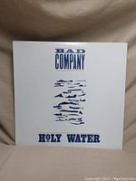 Front cover of Bad Company 'Holy Water' vinyl album with title and band name in blue text on white background.