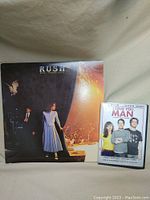 Rush vinyl album "Exit...Stage Left" next to DVD "I Love You, Man" on a fabric background