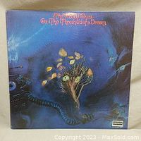 Front cover of The Moody Blues vinyl album 'On the Threshold of a Dream' showing surreal blue artwork with tree and mechanical elements.