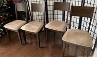 Four espresso wood dining chairs with tan cushions shown from front at an angle on wooden floor with decorative folding screen in background.