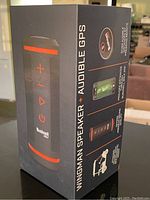 Packaging box showing front and side view of the Bushnell Wingman speaker, highlighting brand, controller buttons, and features including audible GPS and magnetic cart mount.