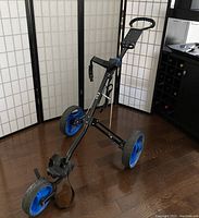 Front right side view of the Power Bilt golf push cart, showing the handle, two large blue rear wheels, and the front wheel attached to the black frame.