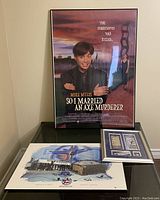 Photo showing the framed movie poster 'So I Married an Axe Murderer' standing upright, with the Toronto 2000 All Star Game print and the framed replica ticket set placed on a glass table below it.