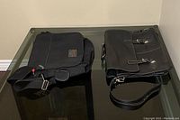 Both messenger bags side by side on a glass table, showing canvas and leather materials.