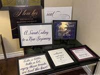 Photo of eight framed wedding signs with various wedding-related messages arranged on a floor against a wall.