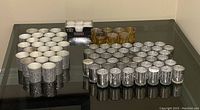 Lot displayed on a glass table showing grouped silver votive holders with white candles and smaller group of gold votive holders.