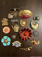 Full view of all 17 vintage brooches arranged on dark surface, showing variety of colors, shapes, and designs.