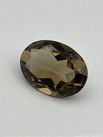 Close-up photo of the faceted smokey quartz gemstone on a white background showing cut angles and color.