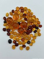 Top-down photo showing a circular arrangement of various polished amber beads in a range of colors from honey yellow to dark brown on a white background.