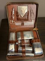 Full view of the open toiletry case showing all silver-tone containers secured by crocodile leather straps along with small scissors, comb, and built-in photo frame.