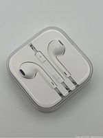 Top view of brand new white Apple earphones neatly arranged in original clear plastic case showing inline controls.
