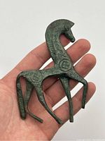 Close-up photo of the hand-held bronze horse figurine showing geometric designs and patina.