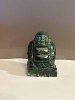 Front view of small green jade Buddha statue showing facial features, robe detail and base.