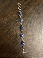 Top-down photo of bracelet laid flat, showing five lapis lazuli stones in circular settings linked with silver-tone metal and toggle clasp at one end.