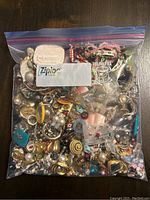 Large freezer bag full of assorted costume jewelry items shown from top view on a dark wooden surface.