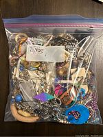 Plastic freezer bag filled with various costume jewelry items including bracelets, necklaces, and earrings in different colors and styles, visible through the bag.