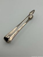Photo showing the full length of the large sterling silver tongs with rounded, spatula-like tips and slight signs of wear.