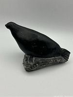 Side angled view of the black soapstone seal sculpture resting on its base, showcasing the smooth body and carved base.