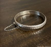 Sterling silver faceted bangle bracelet with safety chain, showing dented area.