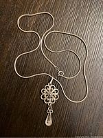 Full view of the sterling silver necklace with chain and pendant on dark wood surface.