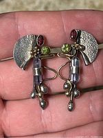 Close-up of both sterling silver earrings showing textured half-circle backing, peridot, garnet, and amethyst gemstones, and gold accenting.