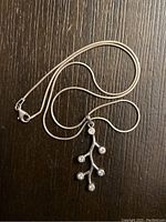 Sterling silver necklace on a dark wooden surface, showing the branch-shaped pendant with six embedded clear gemstones.