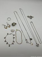 All 10 sterling silver jewellery pieces laid out including rings, bracelets, earrings, chains and pendants. Top right necklace chain is broken and separate.