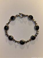 Top view of sterling silver onyx bracelet displaying seven oval black onyx stones and toggle clasp.