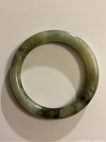 Spinach green stone bangle, top view showing round shape and mottled green color variations.