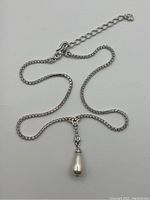 Full view of necklace showing clear rhinestone chain and white teardrop pendant on silver-tone metal.
