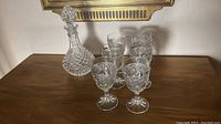 Photo of the antique crystal decanter surrounded by six matching stemmed glasses, showing diamond cut pattern and detailed etched design.