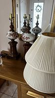 Three antique wood and ceramic lamps with floral design on their ceramic portions, placed on a wooden table with a mirror background.