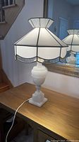 Full view of stained glass shade and marble lamp base on wooden surface reflecting in mirror.
