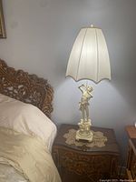 Full view of the antique metal lamp with the musical boy figurine base on a wooden table next to a bed with carved wood details.