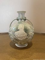 Front view of antique porcelain vase displaying the raised relief profile of a woman and floral decoration, two handles on either side, iridescent finish visible.