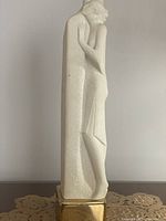 Side view of the tall white sculpture depicting an abstract couple embracing, showing clean lines and brass base.